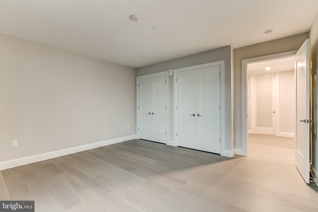 unfurnished bedroom with multiple closets and light hardwood / wood-style flooring