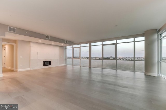 unfurnished living room with a tiled fireplace, expansive windows, a water view, and light wood-type flooring