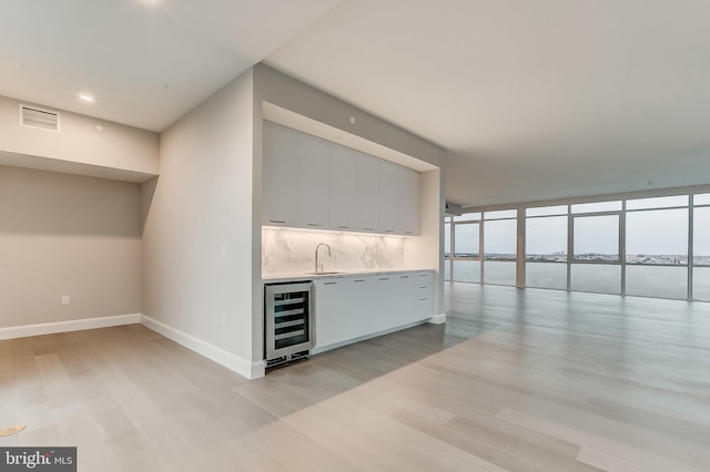 bar with sink, light hardwood / wood-style flooring, backsplash, a water view, and beverage cooler