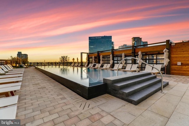 pool at dusk featuring a water view and a patio area