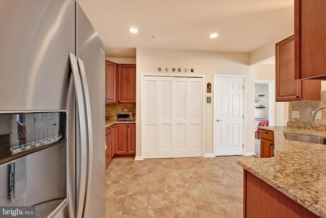 kitchen featuring stainless steel refrigerator with ice dispenser, light stone countertops, sink, and decorative backsplash