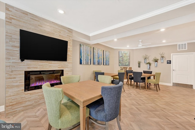 dining room with a tiled fireplace, ceiling fan, crown molding, and light parquet flooring