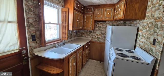 kitchen featuring white electric stove, a healthy amount of sunlight, sink, and wood walls