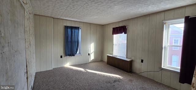 empty room featuring carpet floors, radiator, wooden walls, and a textured ceiling