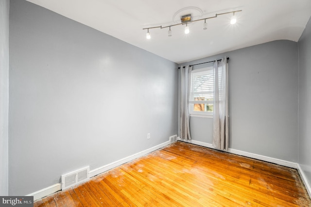 spare room with hardwood / wood-style floors and vaulted ceiling