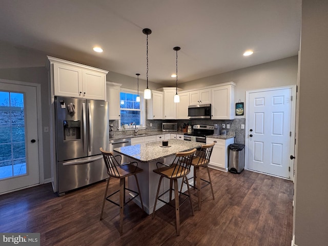 kitchen with dark wood-type flooring, white cabinetry, stainless steel appliances, a center island, and decorative backsplash