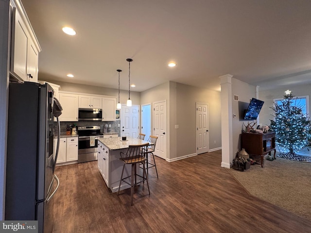 kitchen with appliances with stainless steel finishes, a breakfast bar, decorative light fixtures, white cabinetry, and a center island