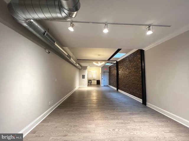 hallway with wood finished floors, baseboards, and brick wall