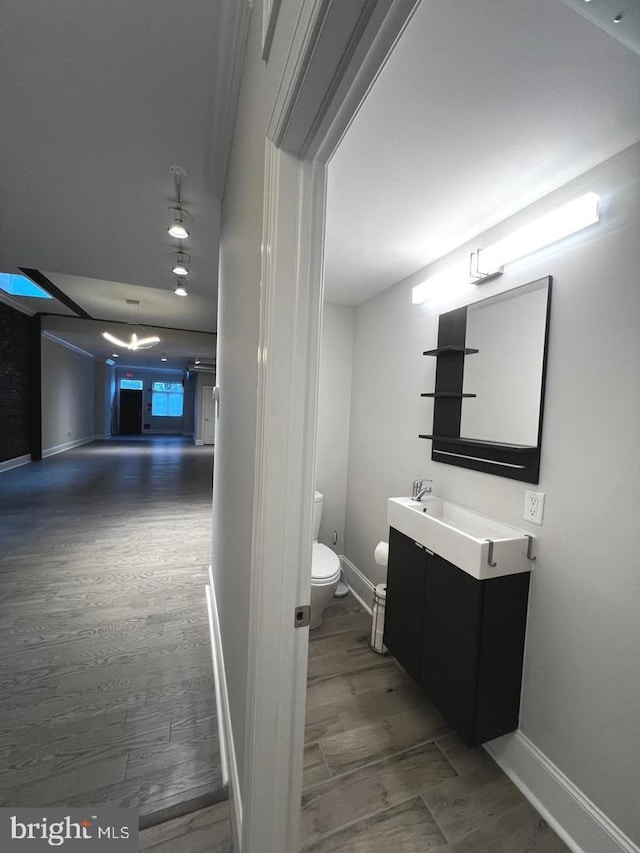 half bathroom featuring vanity, toilet, wood finished floors, and baseboards