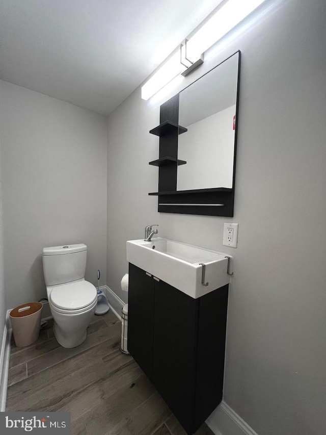 bathroom featuring toilet, vanity, baseboards, and wood finished floors