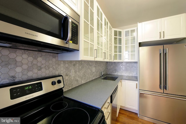 kitchen featuring a sink, white cabinets, glass insert cabinets, and stainless steel appliances