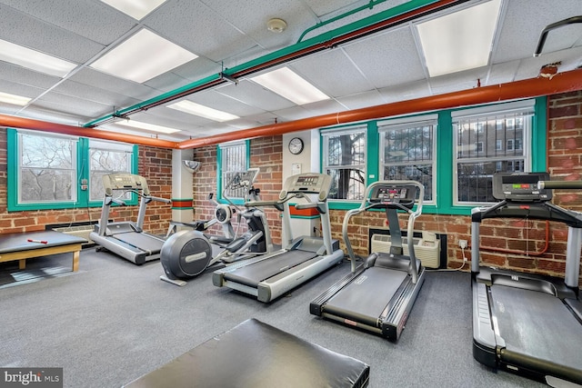 gym with a paneled ceiling and brick wall