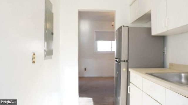 kitchen with stainless steel refrigerator, white cabinetry, and sink