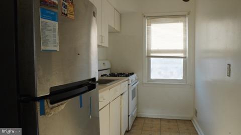 kitchen with stainless steel refrigerator, light tile patterned floors, white cabinets, and white gas range oven