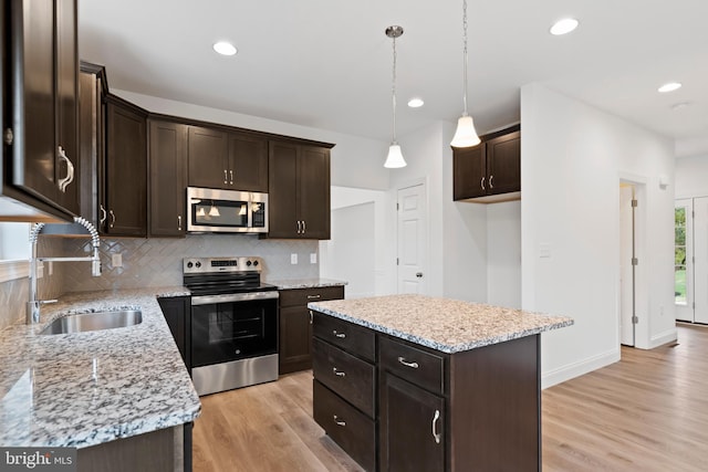 kitchen featuring sink, decorative light fixtures, a center island, appliances with stainless steel finishes, and light stone countertops