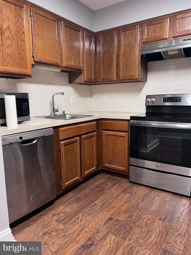 kitchen with appliances with stainless steel finishes, sink, dark hardwood / wood-style floors, and decorative backsplash