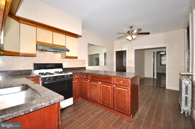 kitchen featuring dark stone counters, decorative backsplash, ceiling fan, kitchen peninsula, and gas range oven