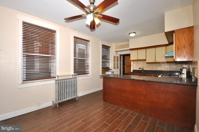 kitchen featuring ceiling fan, dark stone countertops, backsplash, radiator heating unit, and kitchen peninsula