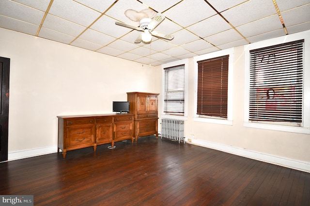 unfurnished office with ceiling fan, a paneled ceiling, dark hardwood / wood-style floors, and radiator