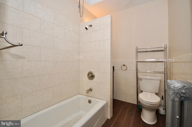 bathroom with tile walls, tiled shower / bath, and toilet