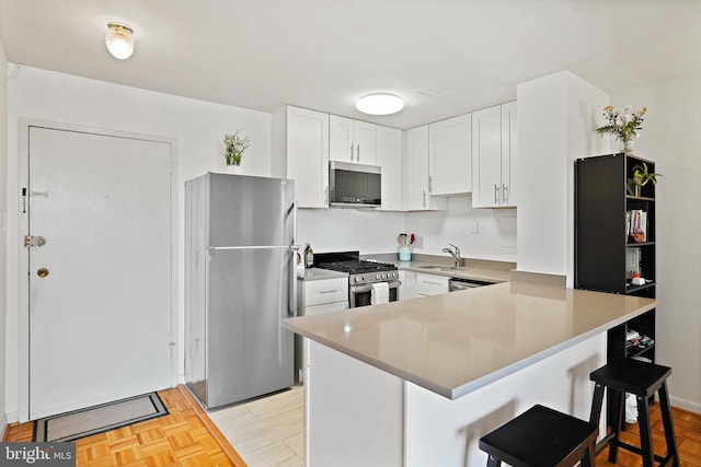 kitchen featuring a kitchen bar, kitchen peninsula, white cabinets, and appliances with stainless steel finishes