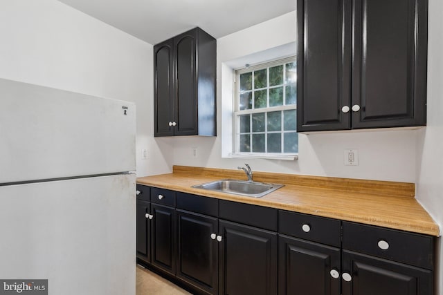 kitchen with wooden counters, sink, and white fridge