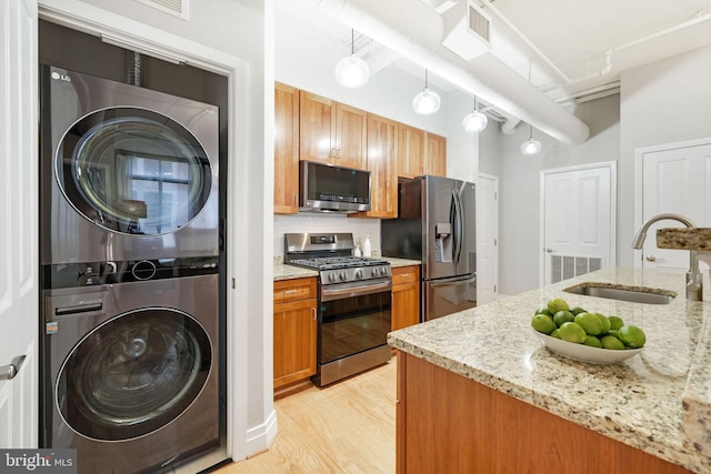 kitchen featuring stacked washer and clothes dryer, sink, light stone counters, decorative light fixtures, and stainless steel appliances