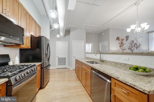 kitchen with appliances with stainless steel finishes, decorative light fixtures, light stone countertops, and sink