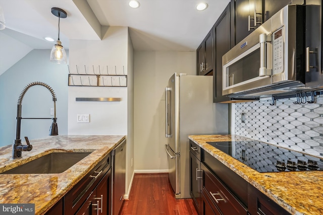 kitchen with appliances with stainless steel finishes, pendant lighting, tasteful backsplash, sink, and light stone countertops