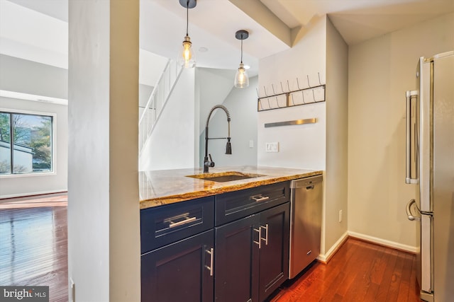 interior space with sink, dark wood-type flooring, hanging light fixtures, stainless steel appliances, and light stone countertops