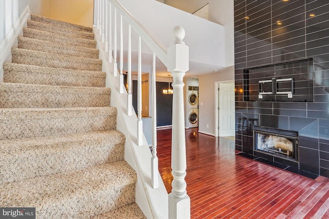 stairs featuring hardwood / wood-style flooring, a multi sided fireplace, stacked washing maching and dryer, and a towering ceiling