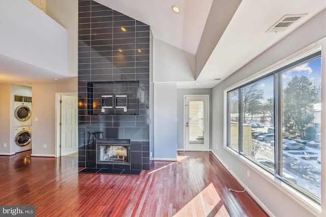 unfurnished living room with a tile fireplace, stacked washing maching and dryer, vaulted ceiling, and wood-type flooring