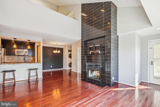 unfurnished living room featuring a chandelier, dark hardwood / wood-style floors, stacked washing maching and dryer, a tiled fireplace, and a high ceiling