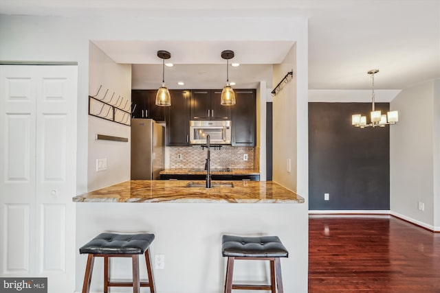 kitchen with hanging light fixtures, appliances with stainless steel finishes, a kitchen breakfast bar, and kitchen peninsula