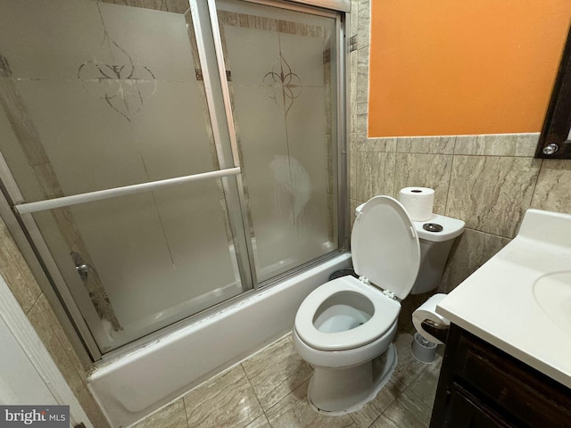 full bathroom featuring enclosed tub / shower combo, vanity, toilet, and tile walls