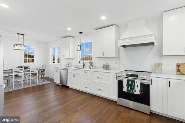 kitchen featuring premium range hood, appliances with stainless steel finishes, pendant lighting, white cabinetry, and sink