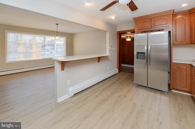 kitchen with a breakfast bar area, tasteful backsplash, light hardwood / wood-style flooring, baseboard heating, and stainless steel fridge