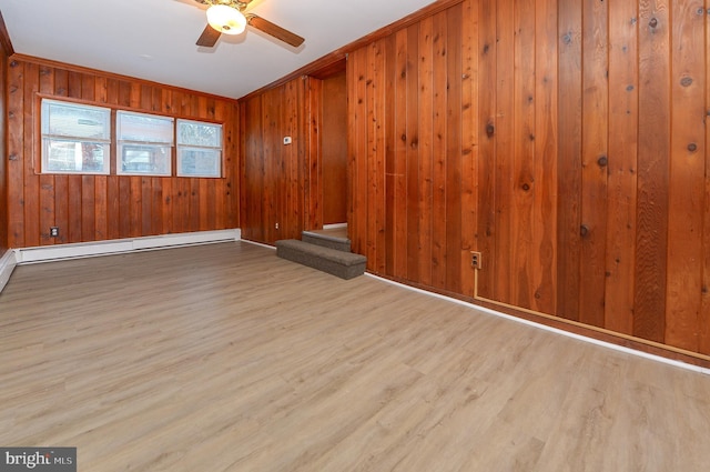 unfurnished room featuring wooden walls, ornamental molding, a baseboard heating unit, ceiling fan, and light hardwood / wood-style flooring