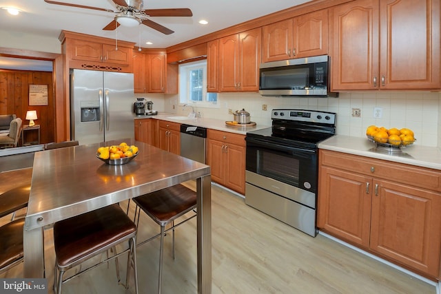 kitchen featuring sink, ceiling fan, appliances with stainless steel finishes, decorative backsplash, and light wood-type flooring