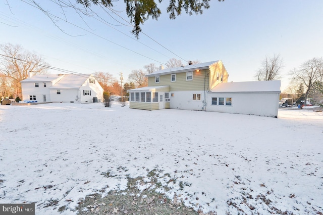 snow covered back of property featuring a sunroom