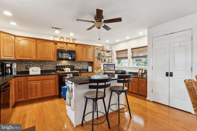 kitchen with a kitchen island, a breakfast bar, light hardwood / wood-style floors, and black appliances