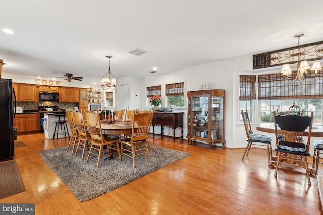 dining room featuring ceiling fan with notable chandelier and light hardwood / wood-style flooring