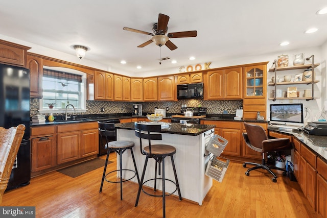 kitchen with sink, a breakfast bar area, a center island, black appliances, and light wood-type flooring