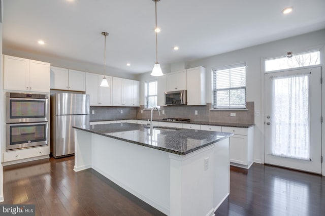 kitchen featuring an island with sink, sink, white cabinets, dark stone counters, and stainless steel appliances