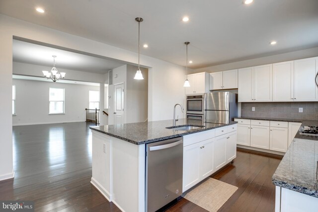 kitchen featuring white cabinetry, dark stone counters, pendant lighting, stainless steel appliances, and a kitchen island with sink