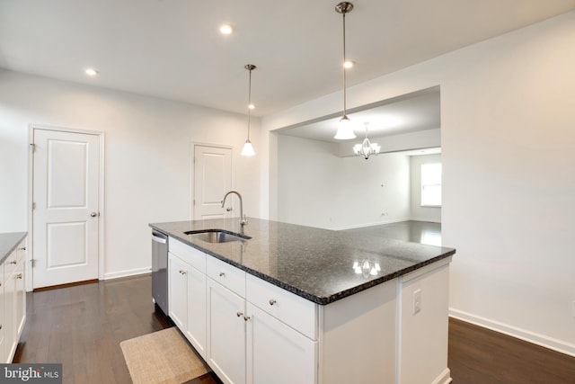 kitchen featuring sink, a kitchen island with sink, white cabinetry, hanging light fixtures, and dark stone counters