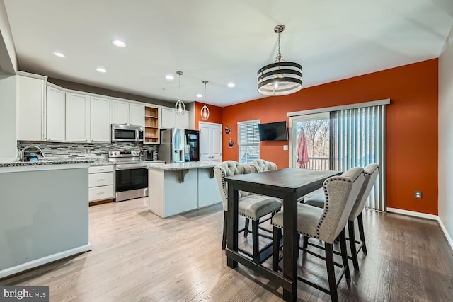 kitchen featuring white cabinetry, hanging light fixtures, stainless steel appliances, a center island, and light stone countertops