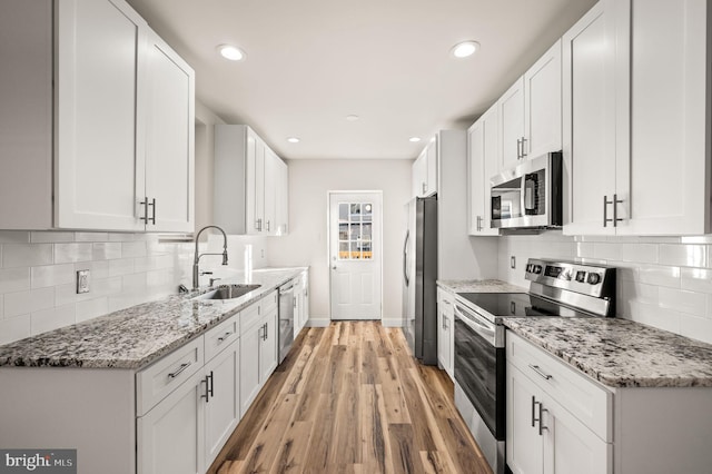 kitchen featuring sink, light hardwood / wood-style flooring, white cabinetry, stainless steel appliances, and light stone countertops