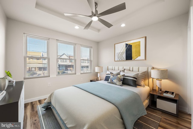 bedroom with ceiling fan, a tray ceiling, and dark hardwood / wood-style flooring