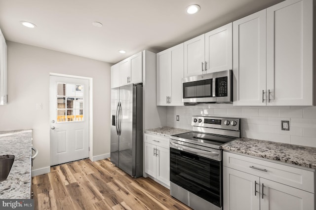 kitchen featuring appliances with stainless steel finishes, white cabinets, backsplash, light stone countertops, and light wood-type flooring